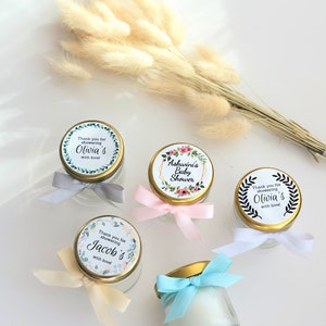 May include: Four small glass jars with gold lids and colorful ribbons. Each jar has a round label with a floral design and text that says "Thank you for showering [name]'s with love!" The names on the labels are Olivia, Olivia, Jacob, and Ashwini.