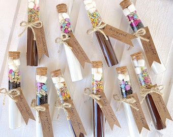May include: Ten glass test tubes filled with various colorful sprinkles, marshmallows, and chocolate. Each tube is tied with twine and a brown paper tag with handwritten text, such as "Love is sweet" and "Baby it's cold outside".