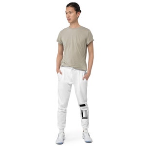 Peut inclure: Pantalon de survêtement blanc avec un motif géométrique noir et gris sur le bas de la jambe. Le pantalon de survêtement a une taille élastique avec cordon de serrage et une coupe décontractée.