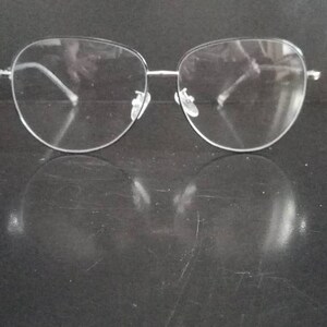 Puede incluir: Gafas de montura transparente con montura de metal plateado. Las gafas están sobre una superficie negra.