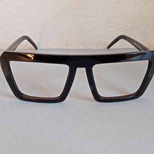 Könnte beinhalten: Schwarze rechteckige Brillenfassung mit geometrischer Form.
