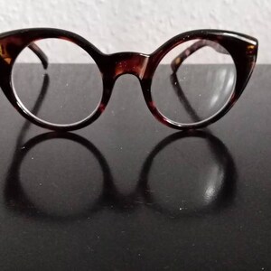 Puede incluir: Gafas de ojo de gato de carey con lentes transparentes. Las gafas están sobre una superficie negra.