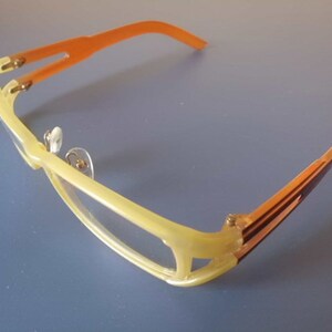 Puede incluir: Un par de gafas amarillas y naranjas con lentes transparentes. Las gafas tienen un diseño único con un marco delgado y curvo.