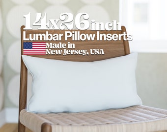 May include: A white lumbar pillow insert on a wooden chair. The pillow is 14x26 inches and made in New Jersey, USA. The text "14x26 inch Lumbar Pillow Inserts Made in New Jersey, USA" is displayed above the pillow. The American flag is displayed to the left of the text.