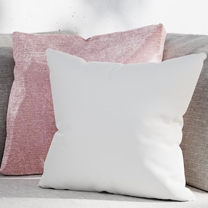 May include: Two decorative throw pillows, one white and one pink with a shimmery texture. The pillows are arranged on a gray couch.