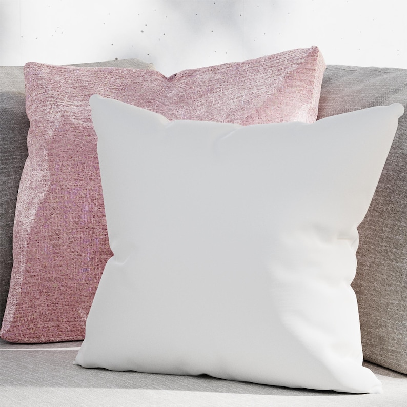 May include: Two decorative throw pillows, one white and one pink with a shimmery texture. The pillows are arranged on a gray couch.