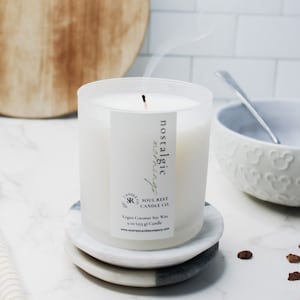 May include: A white frosted glass candle with a black label that reads "nostalgic mornings" and "Soul Rest Candle Co.". The candle is on a white and gray marble coaster. The candle is made with vegan coconut soy wax and is 9 ounces.