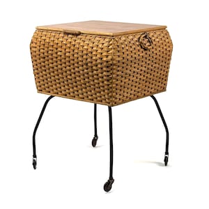 Könnte beinhalten: Gewebte Aufbewahrungstruhe aus Korbgeflecht mit Holzdeckel und schwarzen Metallbeinen. Die Truhe ist rechteckig mit abgerundeten Ecken und einem Griff an der Seite. Sie hat vier gebogene Beine mit kleinen Rädern.