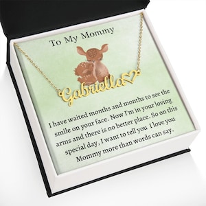 May include: A gold necklace with a heart charm and the name "Gabriella" on it. The necklace is in a white box with a green background and a message that reads "To My Mommy I have waited months and months to see the smile on your face. Now I'm in your loving arms and there is no better place. So on this special day, I want to tell you I love you Mommy more than words can say."