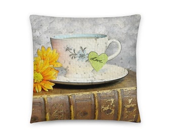 May include: A teacup with a green heart-shaped tea bag that says "Love" sits on a stack of old books with a yellow flower next to it.