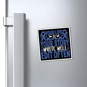 Puede incluir: Un imán rectangular con el texto "YOUR LIFE IS YOUR STORY WRITE WELL EDIT OFTEN" en blanco y azul. El imán tiene un fondo negro y está decorado con cintas azules y una mariposa.