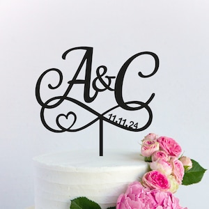 Könnte beinhalten: Schwarzer Acryl-Kuchentopper mit den Buchstaben A & C, die in einem Unendlichkeitszeichen ineinander verschlungen sind. Ein kleines Herz ist im Design enthalten. Das Datum 11.11.24 ist unter den Buchstaben geschrieben.