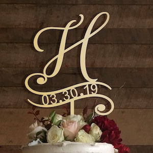 May include: Gold wedding cake topper with a cursive letter H and the date 03.30.19.