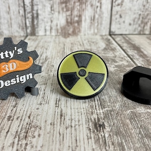 May include: Three 3D printed objects: a black gear with the text "Ditty's 3D Design" and an orange mustache, a yellow and black radiation symbol, and a black plastic cable organizer.