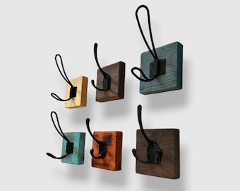 May include: A set of six wall-mounted coat hooks, each featuring a square wooden base in various stained finishes including natural, brown, blue, and turquoise, paired with a black metal double-prong hook secured by a central mounting plate.