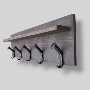 May include: A dark brown wooden coat rack with a shelf and five black metal hooks. The hooks are shaped like nails with a curved top.