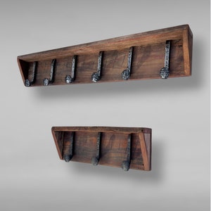 Puede incluir: Dos percheros de pared hechos de madera recuperada de color marr&oacute;n oscuro, cada uno con un estante horizontal y varios ganchos de metal negro con un acabado texturizado y martillado. El perchero m&aacute;s grande tiene seis ganchos y el peque&ntilde;o tres.