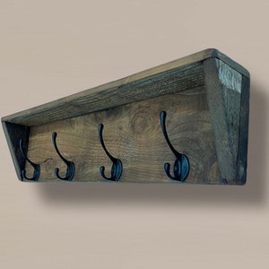 May include: A rustic wooden coat rack with a shelf and five black metal hooks. The rack is angled and has a distressed wood finish.