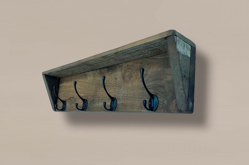 May include: A rustic wooden coat rack with a shelf and five black metal hooks. The rack is angled and has a distressed wood finish.