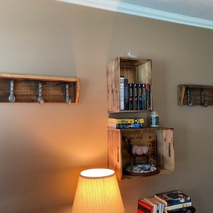 May include: Three wooden shelves with hooks, one with books, one with a deer figurine, and one empty. The shelves are made of reclaimed wood and have a rustic look.