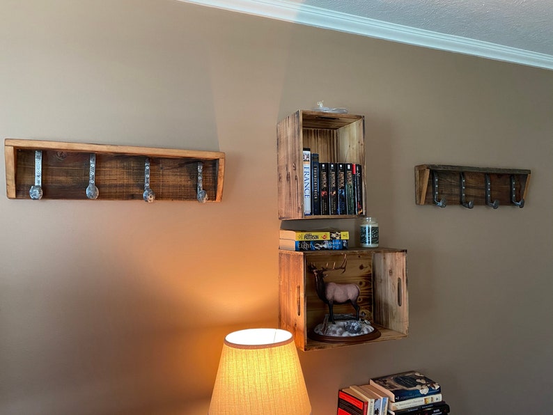 May include: Three wooden shelves with hooks, one with books, one with a deer figurine, and one empty. The shelves are made of reclaimed wood and have a rustic look.