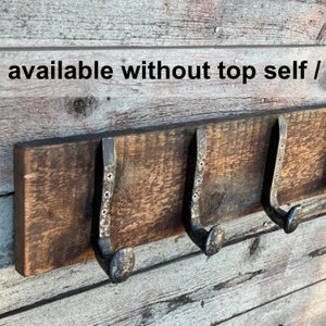Puede incluir: Un perchero de pared con una tabla de madera rectangular de color marr&oacute;n oscuro y cuatro ganchos de metal oscuro. El texto "Also available without top self / borders" es visible arriba y las letras "AHT" est&aacute;n en la esquina.