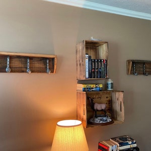 Puede incluir: Dos estantes de pared rectangulares de madera con ganchos de metal en forma de cuchara y dos estantes de caja de madera apilados. Los estantes de pared presentan madera te&ntilde;ida oscura y cuatro ganchos de metal plateado cada uno.