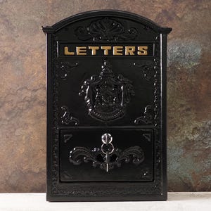 May include: Black cast iron letterbox with intricate detailing and the word "LETTERS" in gold lettering. The letterbox features a decorative crest and a key lock. A classic design for receiving mail.