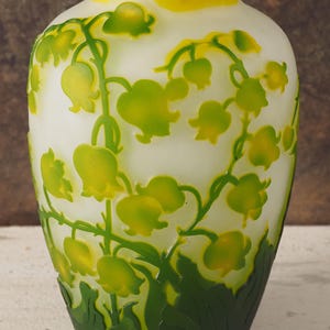 Puede incluir: Un jarr&oacute;n de vidrio blanco con un dise&ntilde;o grabado de flores de lirio de los valles verdes y amarillas.