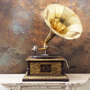May include: An antique gramophone with a large, golden horn. The wooden base is intricately decorated with gold accents and a small label. The record player sits on a white surface against a textured, brown background.