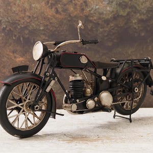 Może przedstawiać: Szczegółowy, czarny i czerwony model motocykla w stylu vintage. Model posiada reflektor, szprychowe koła i bagażnik. Motocykl to element dekoracyjny, prezentujący klasyczny design.