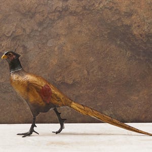 Könnte beinhalten: Detaillierte Skulptur eines Fasanen mit gelbem Schnabel, schwarzem Kopf und braun-rotem Körper. Der Vogel ist in einer Laufhaltung dargestellt, mit seinem langen Schwanz ausgestreckt. Der Hintergrund ist eine strukturierte braune Oberfläche.