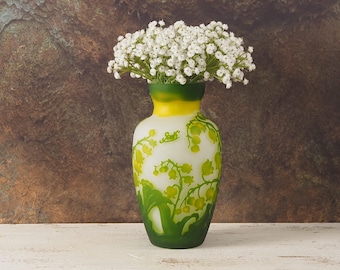 May include: A white ceramic vase with a green and yellow floral design. The vase is filled with a bouquet of white baby's breath flowers.