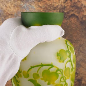 Puede incluir: Un jarr&oacute;n de vidrio blanco y verde con un dise&ntilde;o floral. El jarr&oacute;n tiene una parte superior verde y un cuerpo blanco con un dise&ntilde;o en relieve de flores verdes y amarillas.