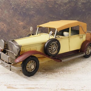 Peut inclure: Modèle de voiture vintage crème, marron et bordeaux. La voiture a une roue de secours, une calandre détaillée et un toit décapotable beige. Les roues sont noires avec des rayons argentés. Objet décoratif.