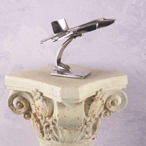 Könnte beinhalten: Ein silbernes Metallmodell eines Kampfjets auf einem Ständer. Der Jet befindet sich in Startposition mit der Nase nach oben.