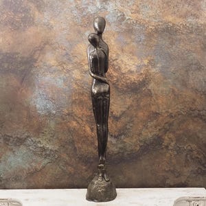 Puede incluir: Una escultura de bronce que representa dos figuras abrazándose. Las figuras están estilizadas con formas suaves y redondeadas y están montadas sobre una base texturizada. La escultura tiene un acabado oscuro y metálico.