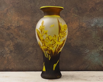 May include: A tall, frosted glass vase with a floral design in shades of yellow and brown. The vase features a wide body and a narrow neck, with a dark brown base and rim. The floral pattern includes detailed leaves and flowers.