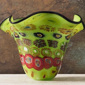 Könnte beinhalten: Eine dekorative Glasvase mit einem ausgestellten, gerüschten Rand. Die Vase ist hauptsächlich limettengrün mit bunten floralen und abstrakten Mustern in Rot, Braun und Weiß. Der Rand ist schwarz umrandet.