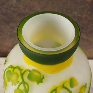 Puede incluir: Jarr&oacute;n de vidrio blanco esmerilado con un borde verde y amarillo. El jarr&oacute;n est&aacute; decorado con un patr&oacute;n floral de flores de lirio de los valles verdes.
