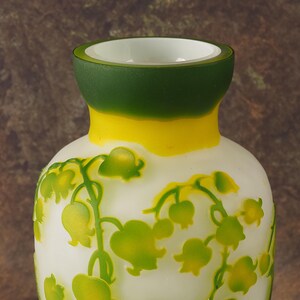 Puede incluir: Un jarr&oacute;n de vidrio blanco con un borde verde y amarillo. El jarr&oacute;n est&aacute; decorado con un patr&oacute;n floral de lirios del valle.