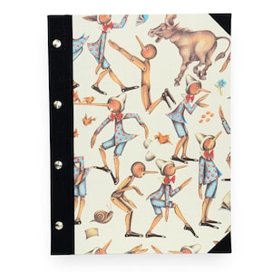 Può includere: Un quaderno con dorso nero e rivetti argentati. La copertina presenta un'illustrazione stravagante di figure di Pinocchio in varie pose, insieme a un asino e altri elementi su sfondo crema.