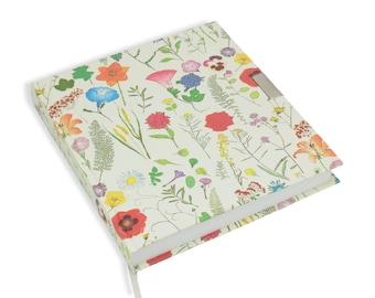 May include: A white journal with a floral pattern featuring a variety of colorful flowers and green leaves. The journal has a silver clasp.