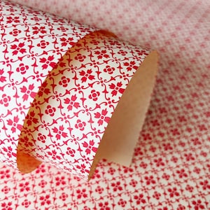 Könnte beinhalten: Eine Rolle gemustertes Papier mit einem sich wiederholenden floralen Design in Rot auf weißem Hintergrund. Das Papier ist teilweise abgerollt und zeigt das Innere der Rolle. Das Muster ist auf dem abgerollten Teil und im Hintergrund sichtbar.