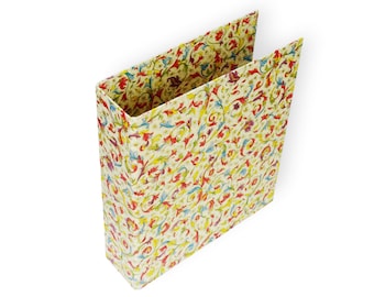 May include: A rectangular paper gift bag with a colorful floral pattern. The bag's design features a cream background with red, yellow, blue, and green floral elements. The bag is open at the top, revealing the interior.