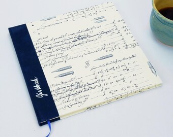 May include: A hardcover notebook with a cream-colored cover featuring handwritten script and pen illustrations. The spine is navy blue with the word "Gastrobule" in white script. A blue ribbon bookmark is attached.