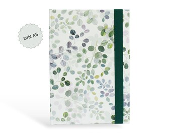 May include: A DIN A5 notebook with a white cover featuring a watercolor-style pattern of green and muted purple eucalyptus leaves. The notebook is secured with a vertical dark green elastic band that runs along the right side of the front cover.