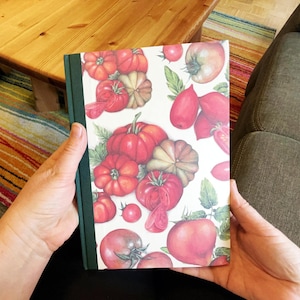 Könnte beinhalten: Ein Notizbuch mit grünem Rücken und einem Einband mit einer Aquarellillustration verschiedener Tomaten und Kürbisse. Das Design umfasst rote, orange und grüne Farbtöne mit detaillierten Darstellungen des Gemüses.