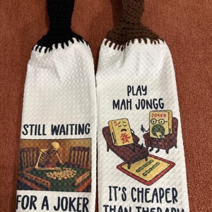 May include: Two white kitchen towels with black and brown crochet tops. One towel reads "STILL WAITING FOR A JOKER" with a skeleton playing Mahjong. The other says "PLAY MAH JONGG IT'S CHEAPER THAN THERAPY" with cartoon Mahjong tiles.