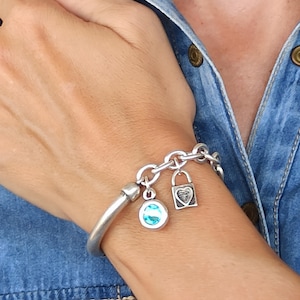 May include: A silver charm bracelet featuring a blue gemstone charm, a heart-shaped lock charm, and a silver chain.